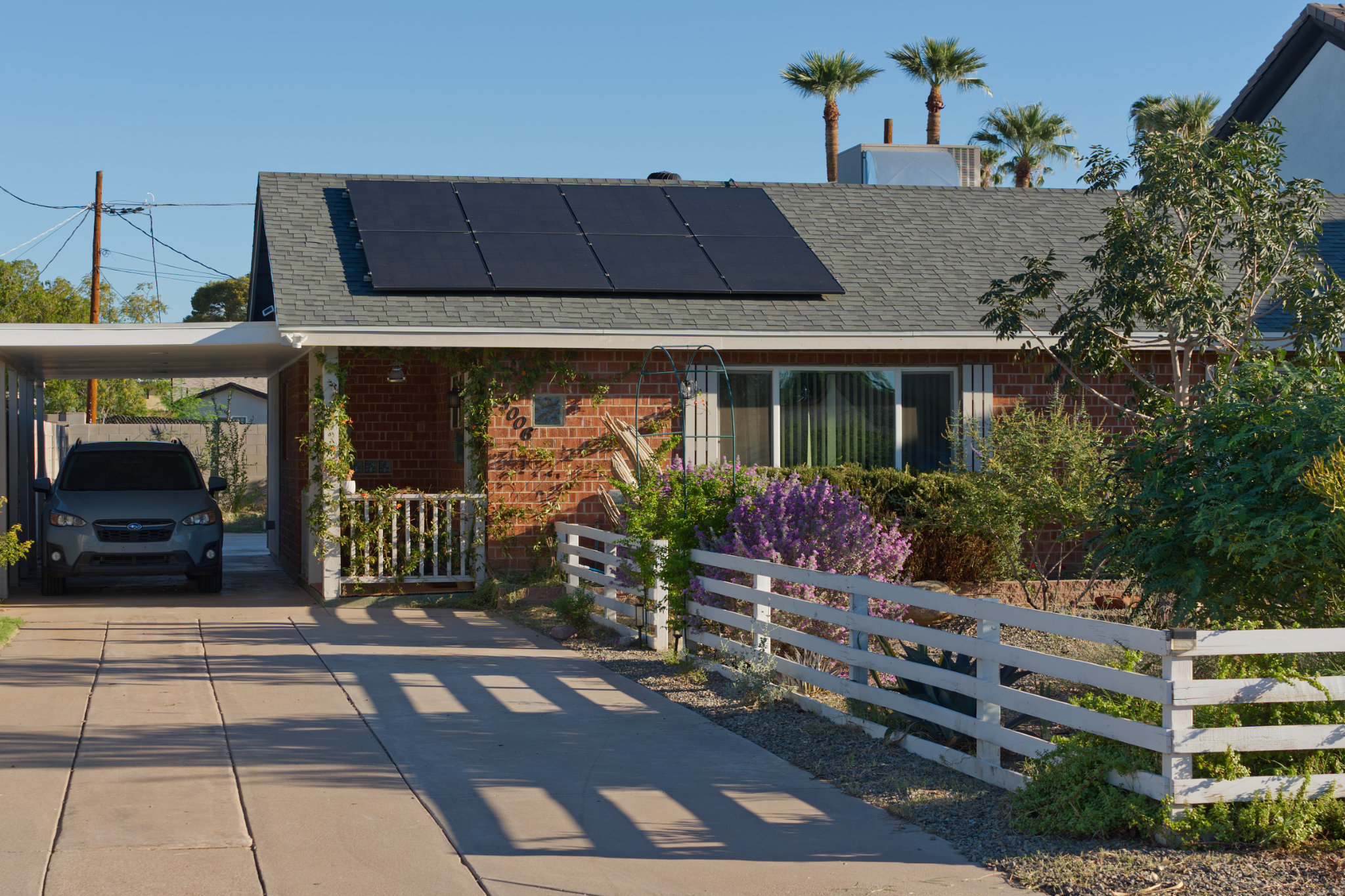 Brick ranch with owned rooftop solar, white fence, and flowering front garden
